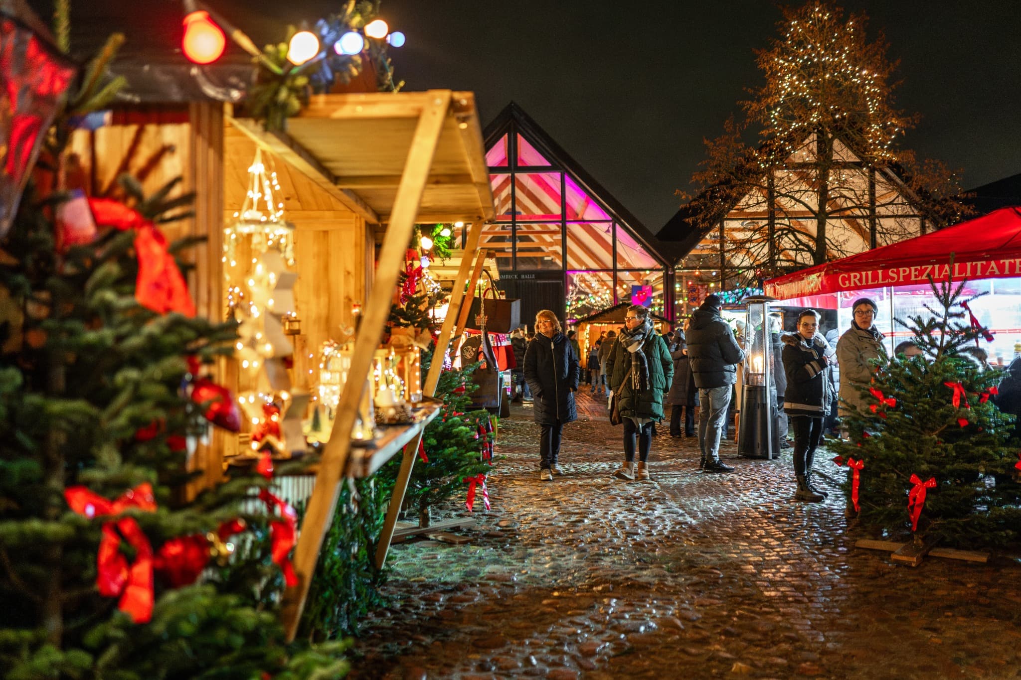Weihnachtlich beleuchtete Holzhütten und Marktbesucher vor dem Feuerwehrmuseum Norderstedt am Abend