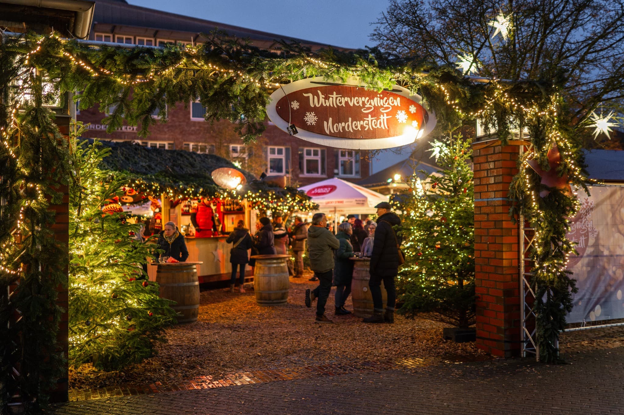 Weihnachtlich beleuchteter Eingang zum Wintervergnügen Norderstedt mit Tannenbäumen und Marktständen